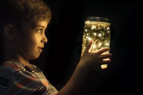 A boy looking a glow worms in a glass